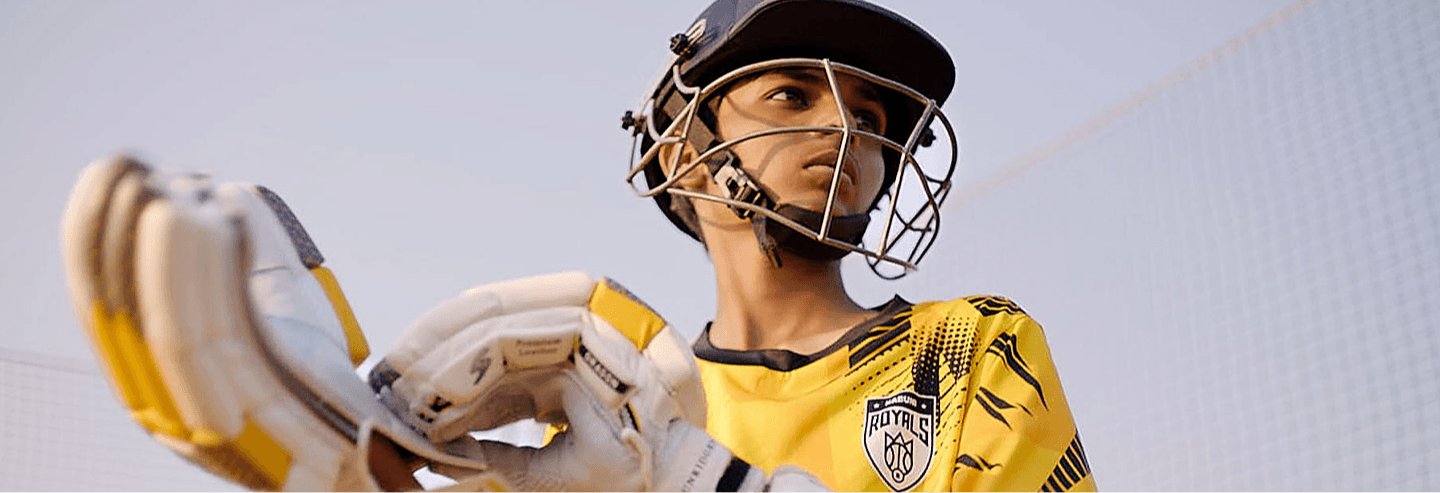 Young cricketer in a yellow Kabuni Royals jersey and batting helmet, holding a bat and gloves